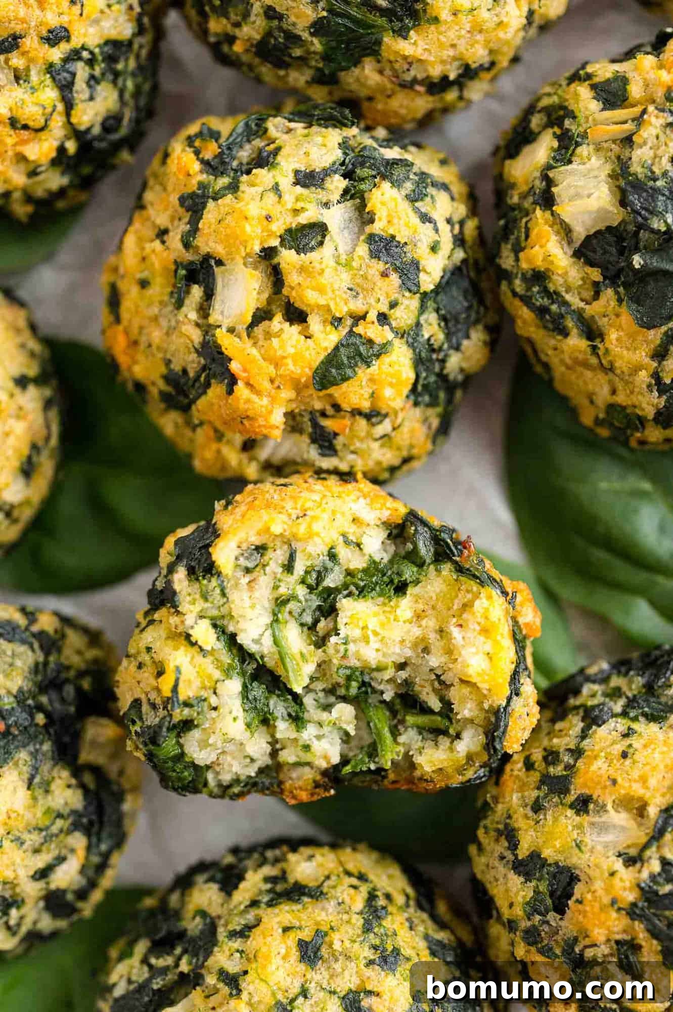 Close up overhead view of assorted spinach balls, one with a bite missing.
