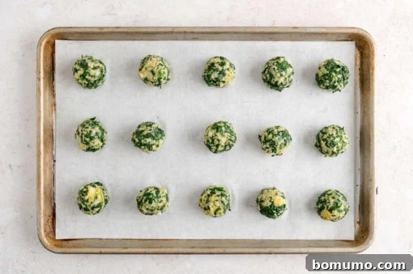 Unbaked spinach balls on a parchment-lined baking sheet.