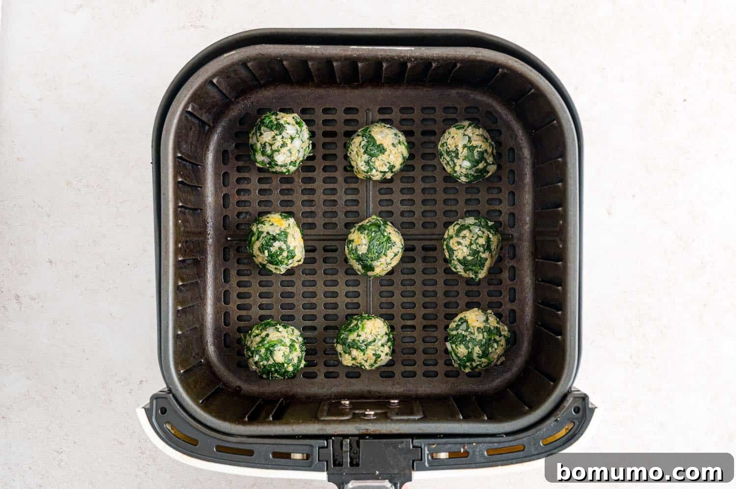 Uncooked spinach balls arranged inside the basket of an air fryer.