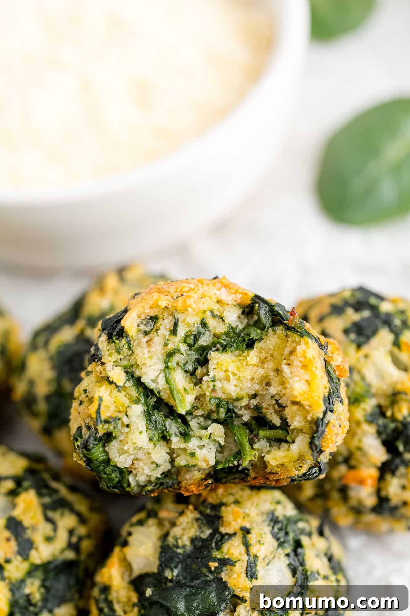 A small pile of spinach balls next to a bowl of dipping sauce.