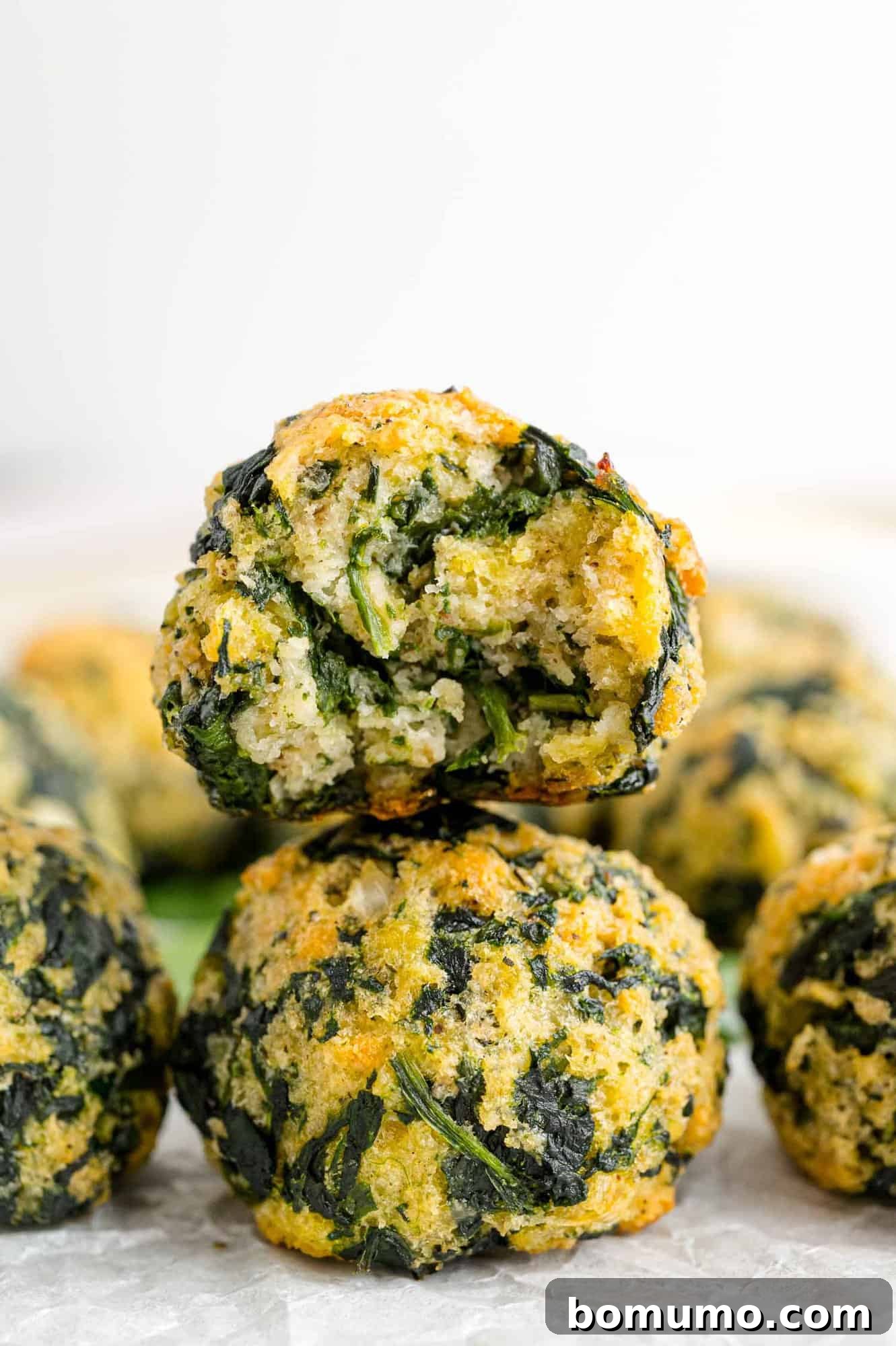 A spinach ball with a bite missing stacked on top of a second spinach ball.