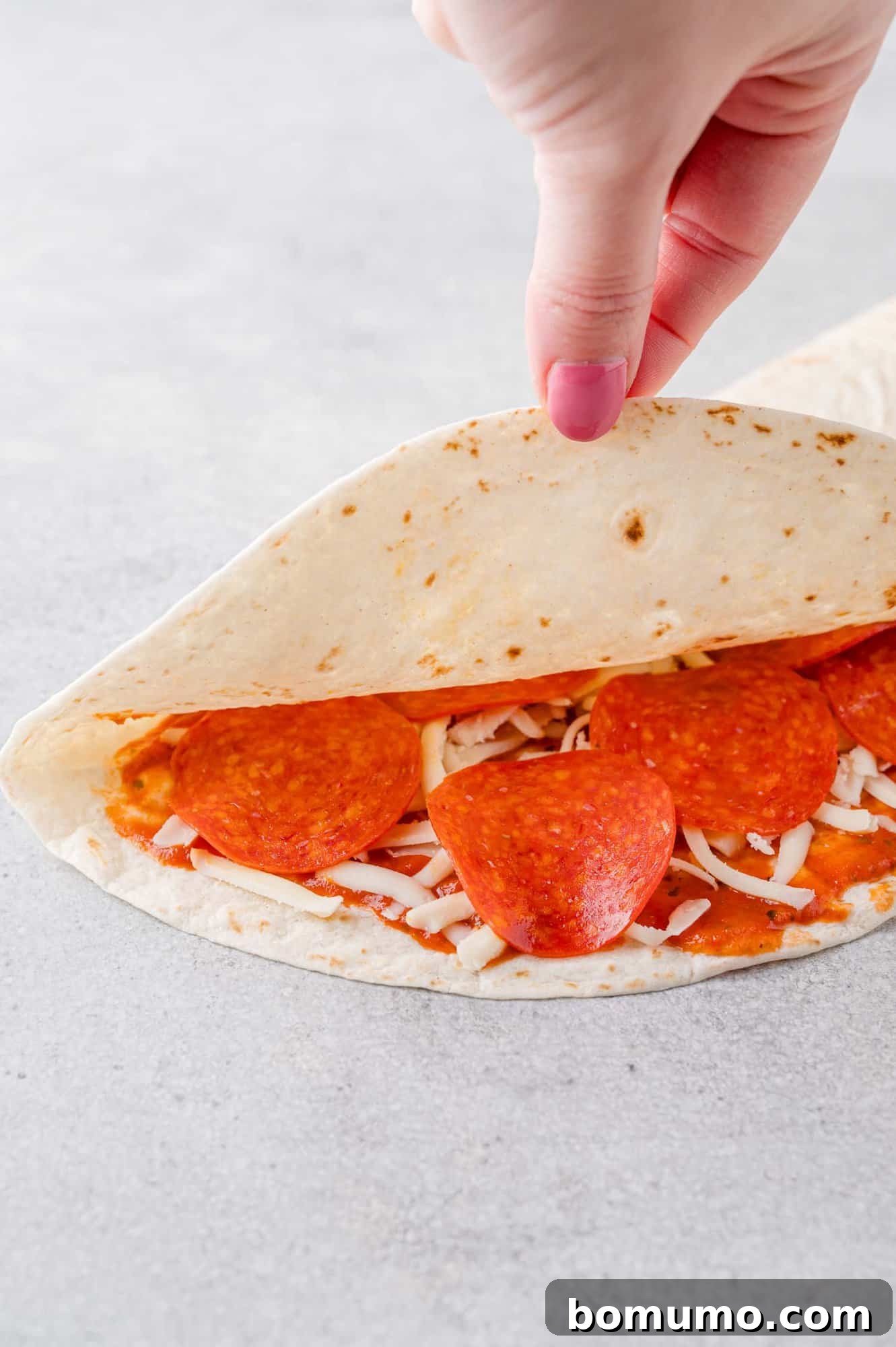 Pizza-Dilla Melt 8 An uncooked quesadilla partially opened to reveal the tantalizing pizza sauce, cheese, and pepperoni filling inside.