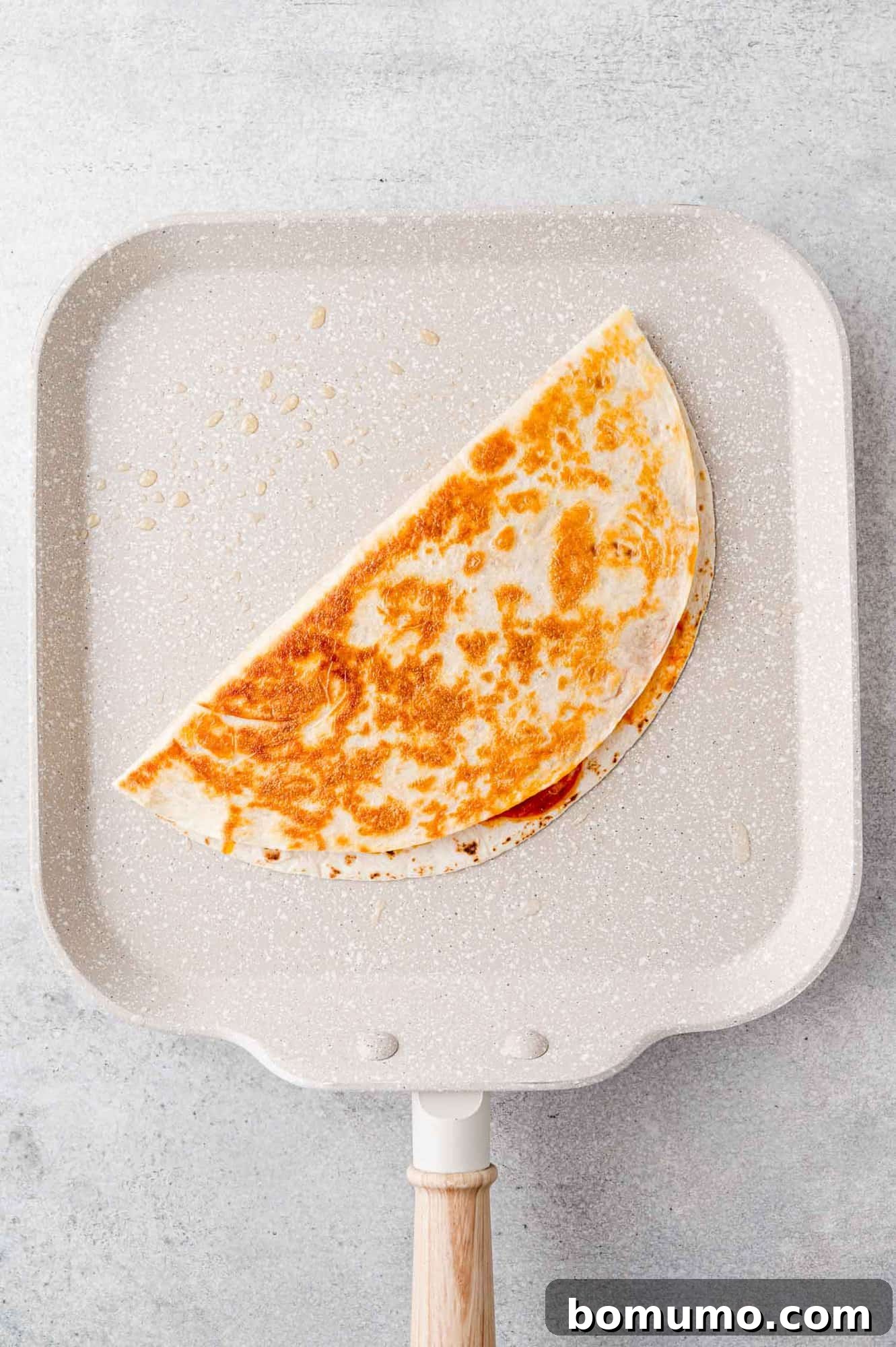 Pizza-Dilla Melt 9 A perfectly golden brown pizza quesadilla sizzling on a griddle, indicating it's almost ready to serve.