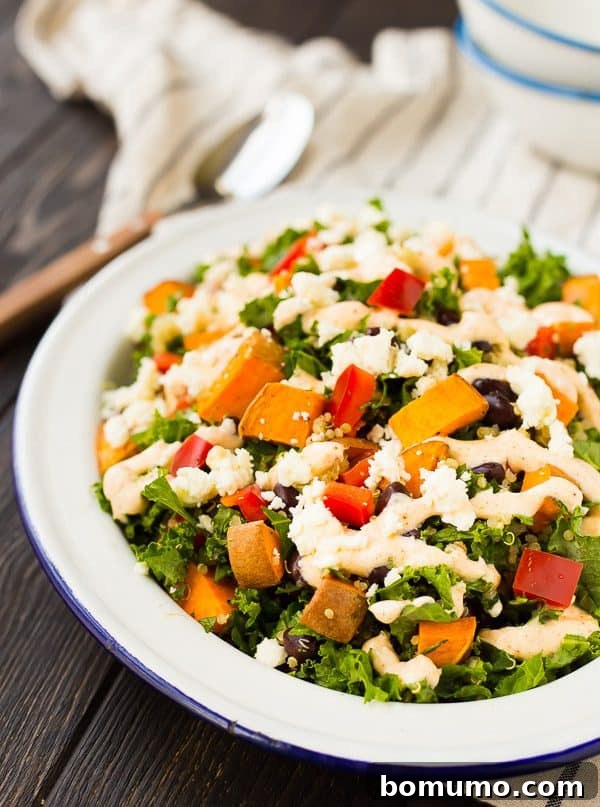 A large bowl of Kale Sweet Potato Salad with a side of creamy dressing, showcasing its vibrant ingredients.