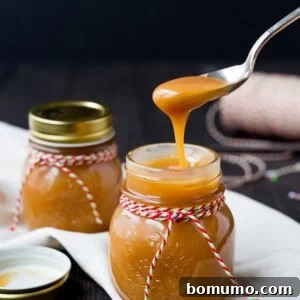 A spoonful of Bourbon Caramel Sauce being held above a jar, illustrating its perfect consistency.