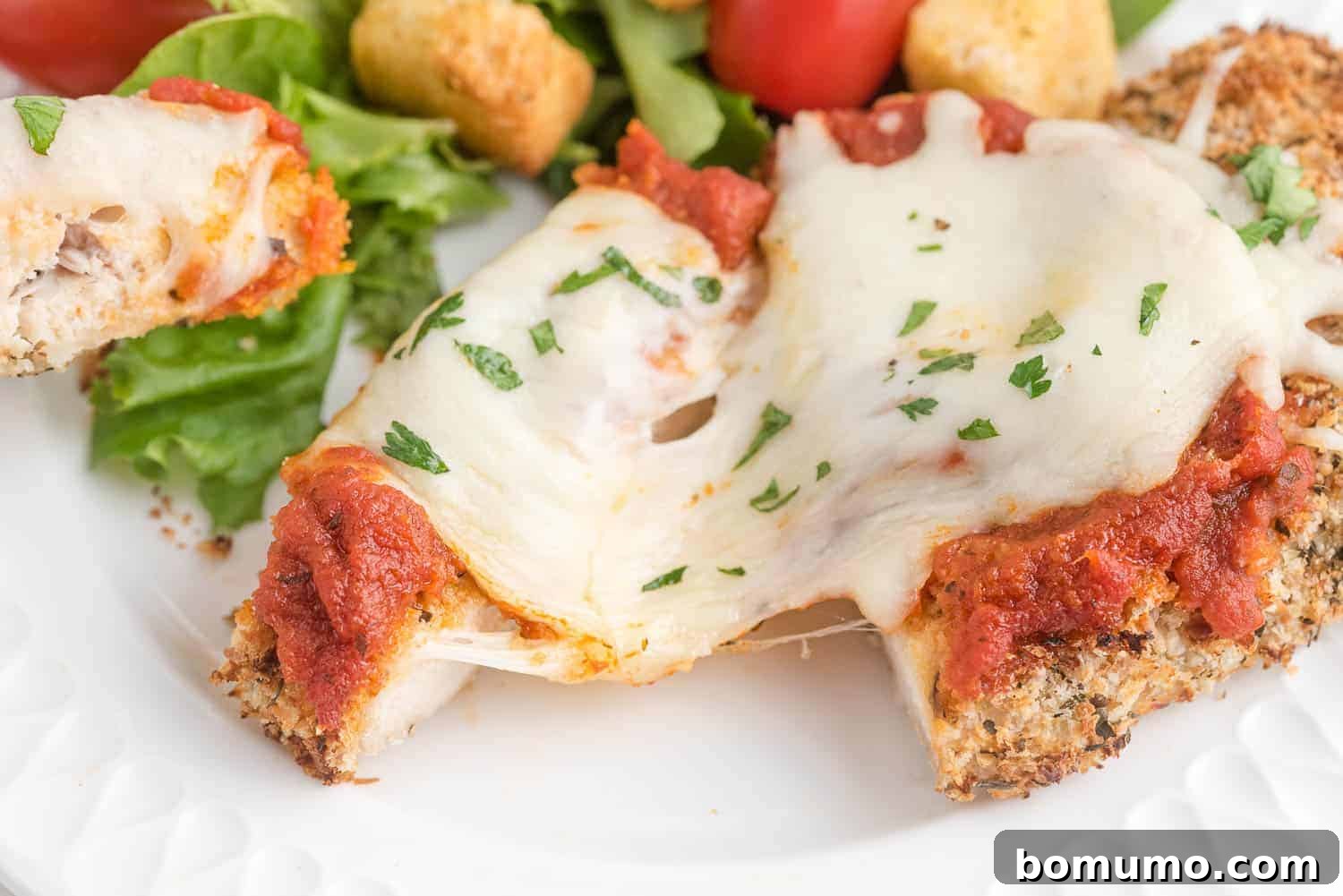 Close-up view of a chicken cutlet topped with perfectly melted, bubbly mozzarella cheese, fresh out of the oven.
