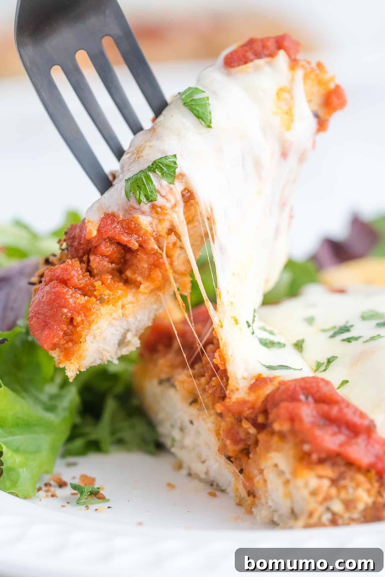 Close up of cheese pull on top of a breaded chicken breast, showing stringy melted mozzarella.