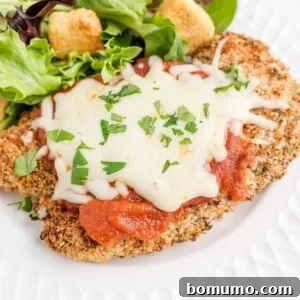 Chicken parmesan on a white plate with a green salad, a healthy and delicious meal.