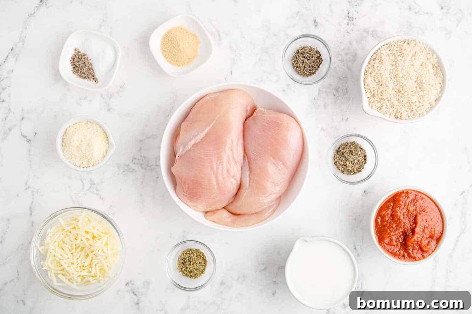 Overhead view of all ingredients needed to make baked chicken parmesan, neatly arranged on a countertop.