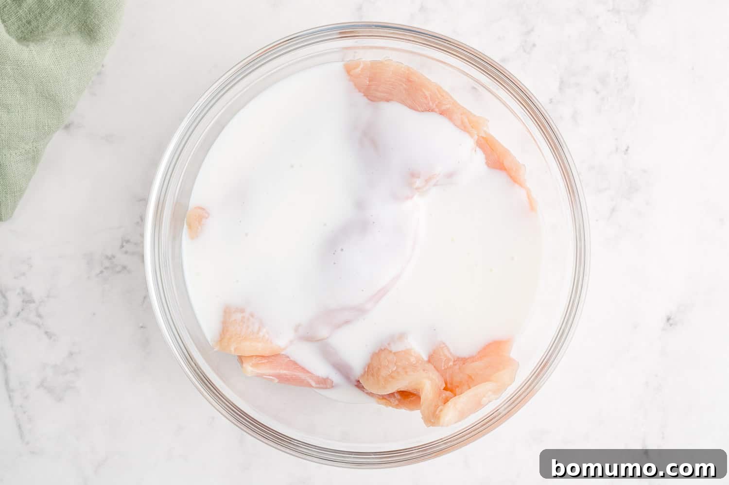 Raw chicken breasts gently soaking in a bowl of creamy buttermilk, ready for the next step in the recipe.