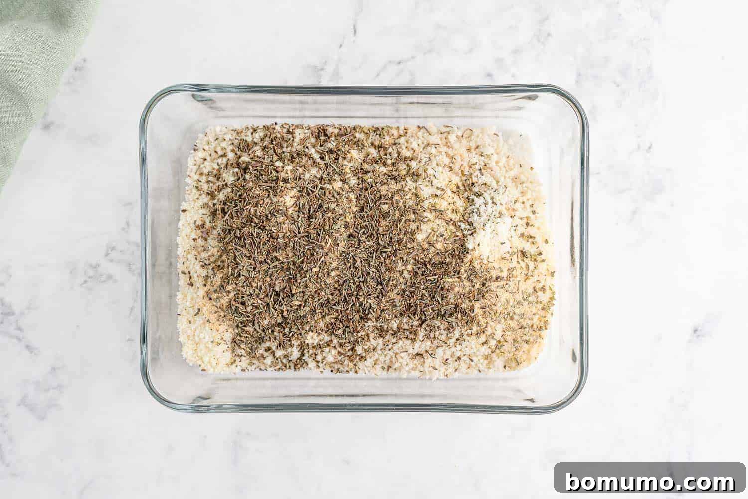 A bowl of panko bread crumbs mixed with dried herbs and spices, forming the crispy coating for the chicken.