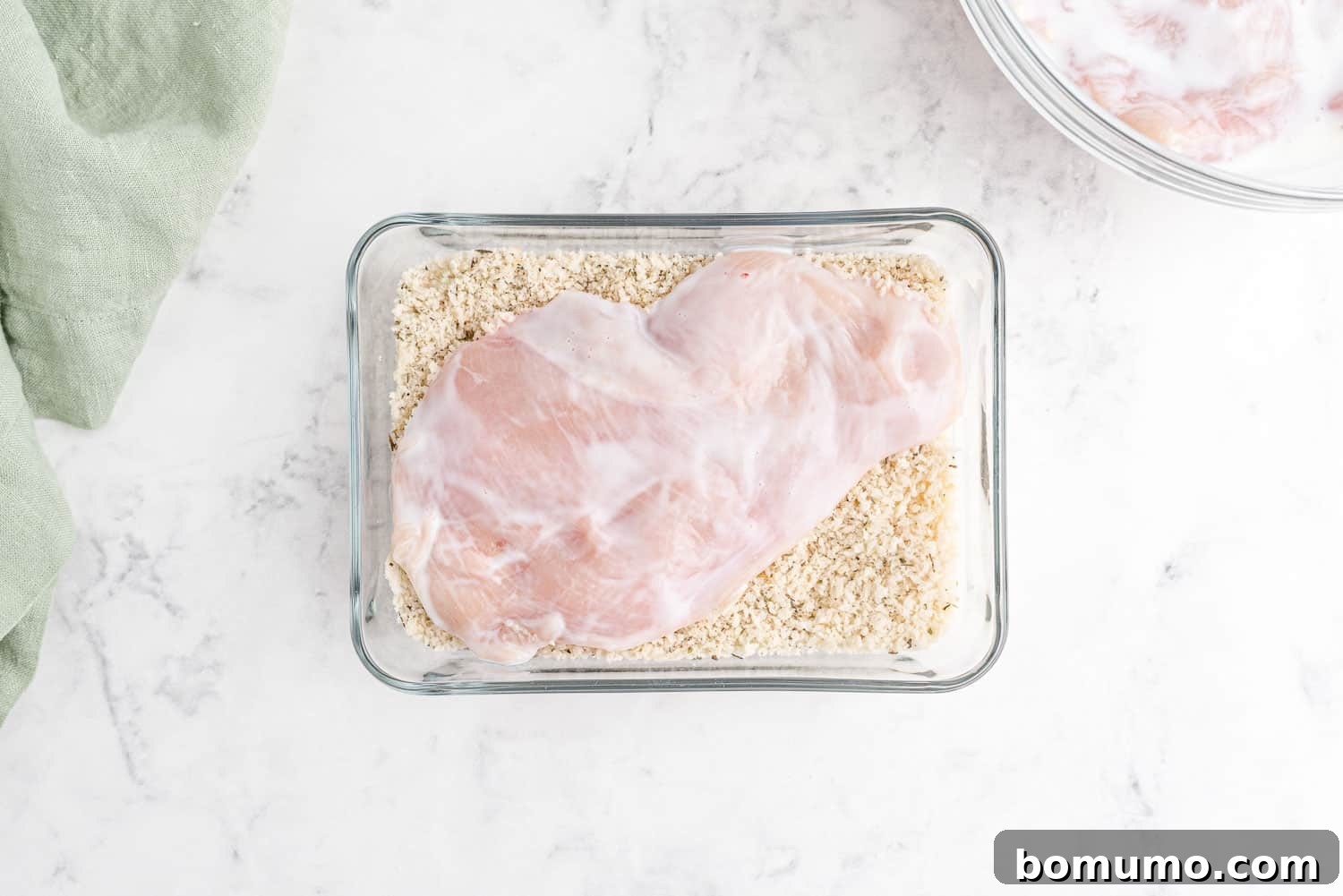 A chicken cutlet being carefully dipped and coated in the seasoned bread crumbs, ensuring full coverage.