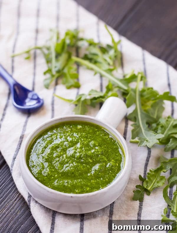 Arugula pesto in a small bowl with a blue spoon, showcasing its smooth texture.