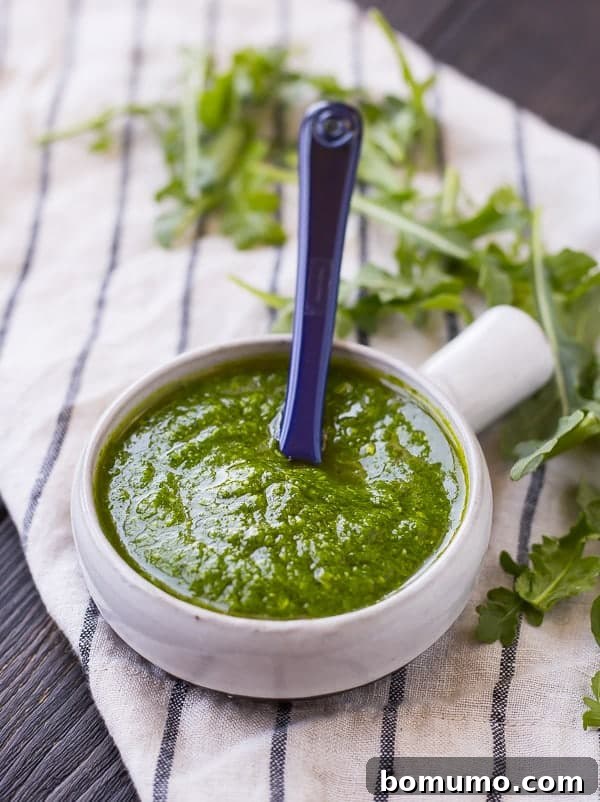 Arugula pesto in a small bowl with a blue spoon, ready to be served.