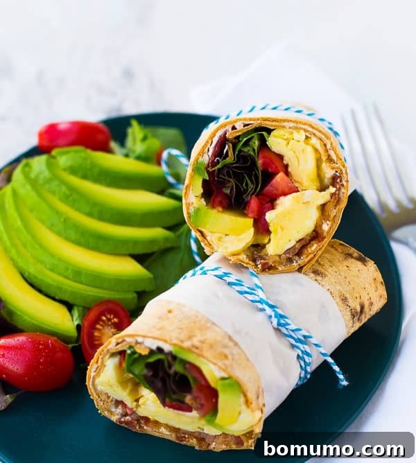 Loaded California Breakfast Wrap 2 California breakfast wrap, cut in half, and bound with parchment and twine, on black plate with sliced avocado and grape tomatoes.