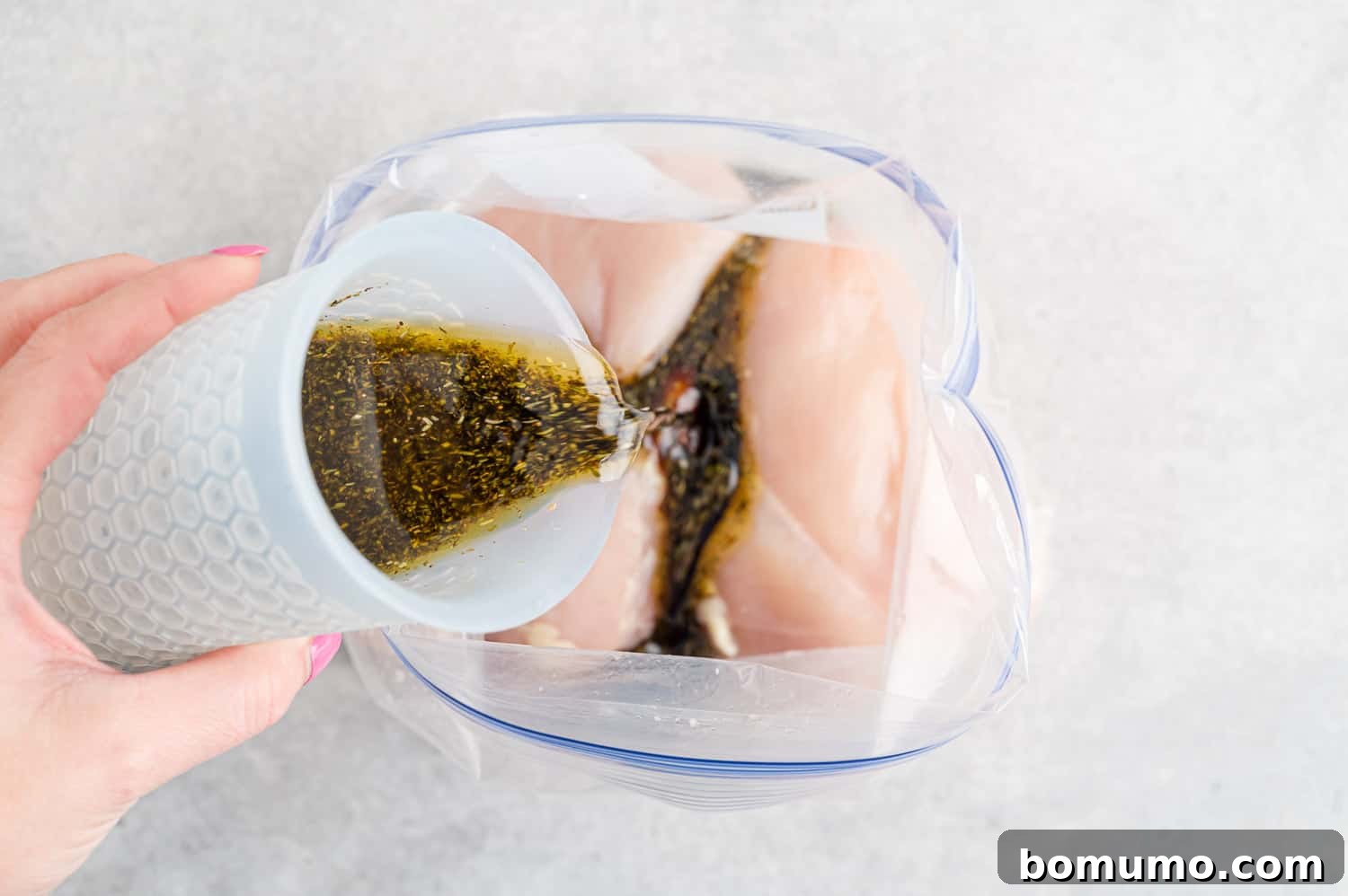 Rich balsamic marinade being generously poured over chicken pieces, ensuring every part is coated for maximum flavor.