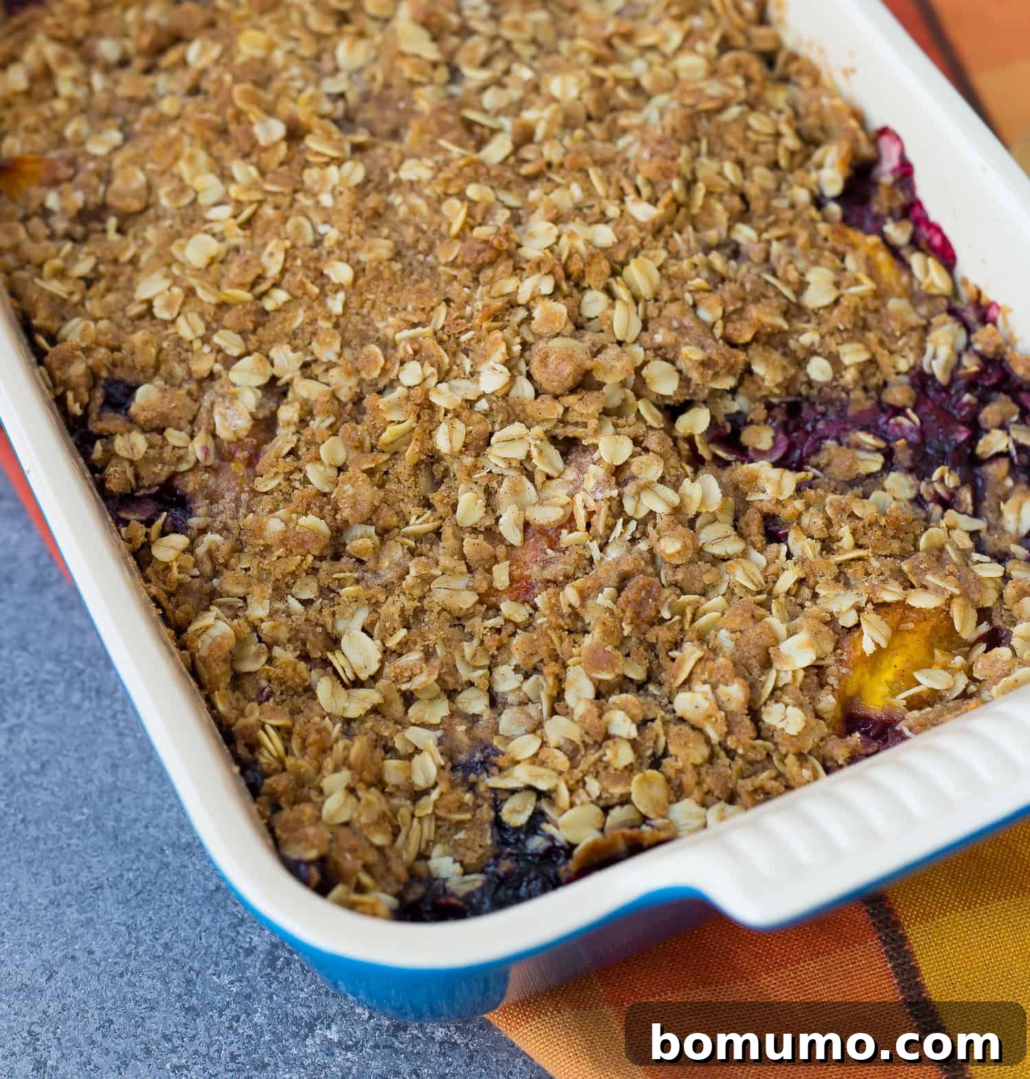 A beautifully baked Peach Blueberry Crisp, fresh out of the oven, with its golden, intact topping. The edges are bubbling, and no scoops have been removed, showcasing its perfect presentation.