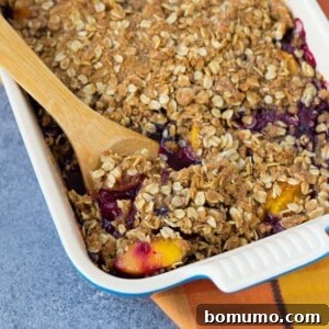 A delightful Peach Blueberry Crisp, presented in a square baking dish with a wooden serving spoon, ready to be enjoyed.