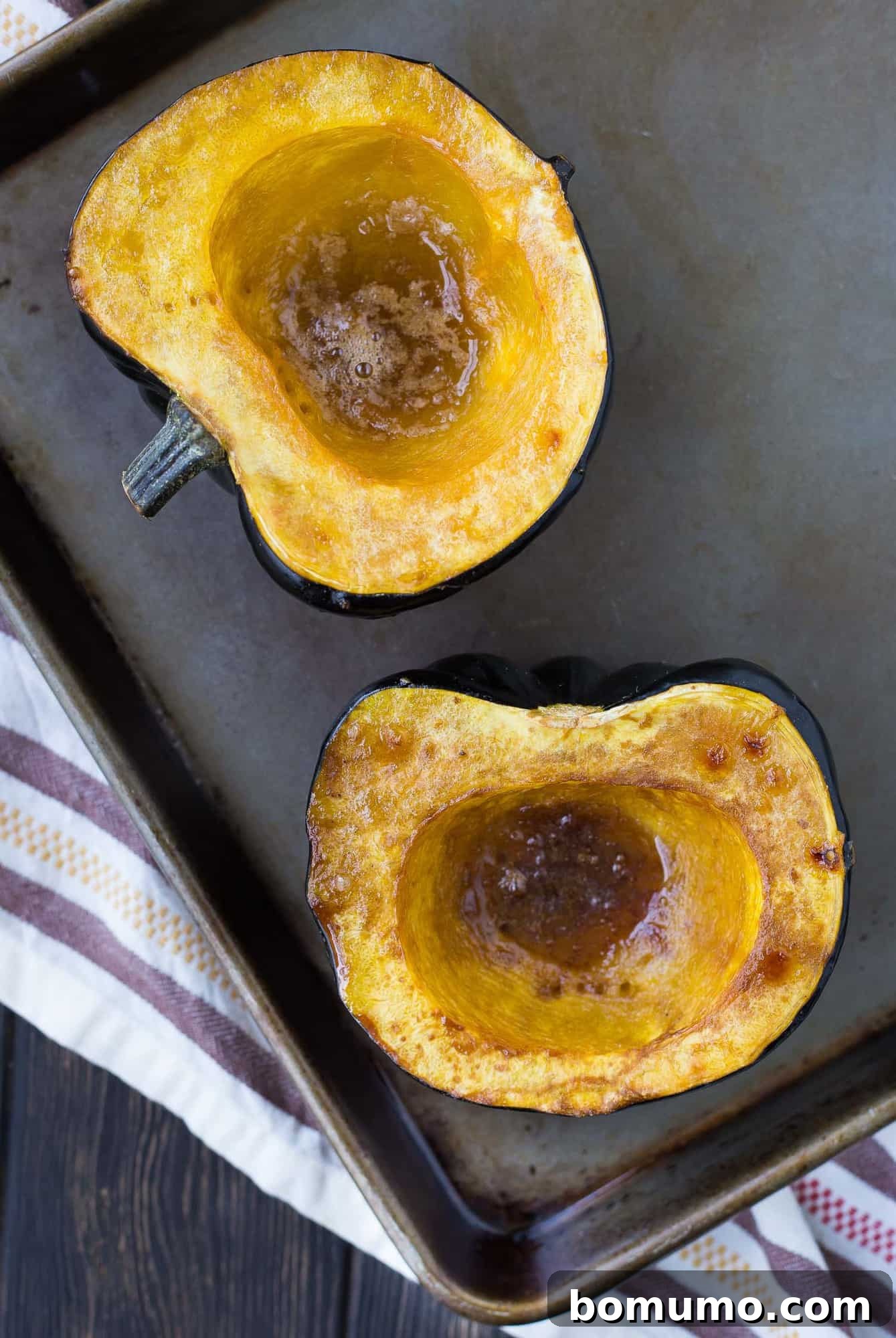 Two halves of roasted acorn squash with brown sugar and butter, on a baking sheet.
