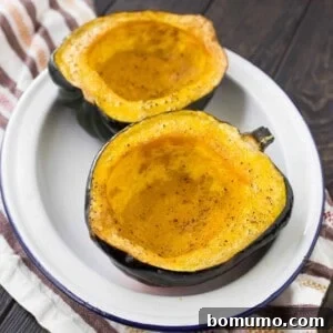 Two acorn squash halves on a white platter, both have been roasted and seasoned with salt and pepper.