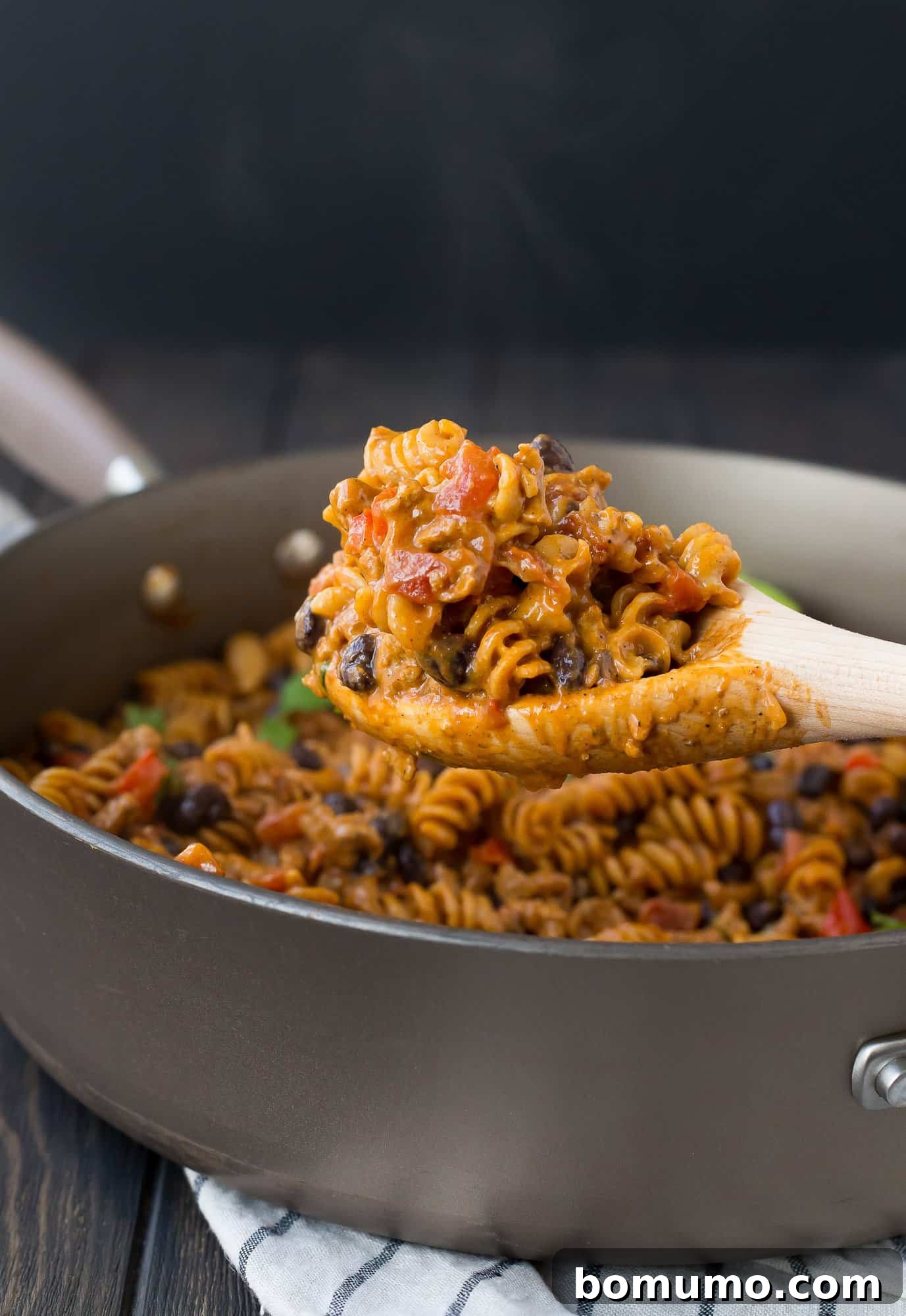 A serving of creamy One Pot Taco Pasta being scooped from a large skillet, highlighting the rich texture and vibrant ingredients.