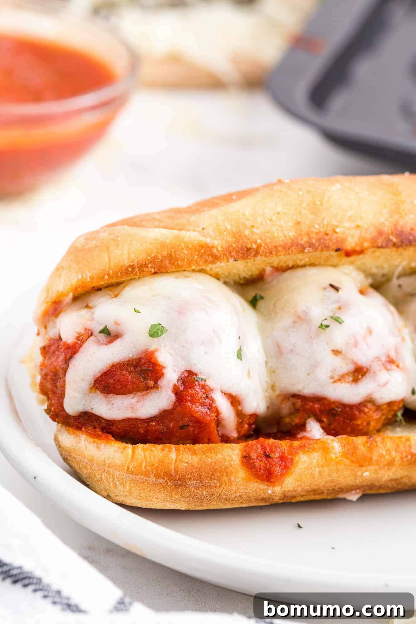 Close up of a meatball sub, sauce dripping over the bun.