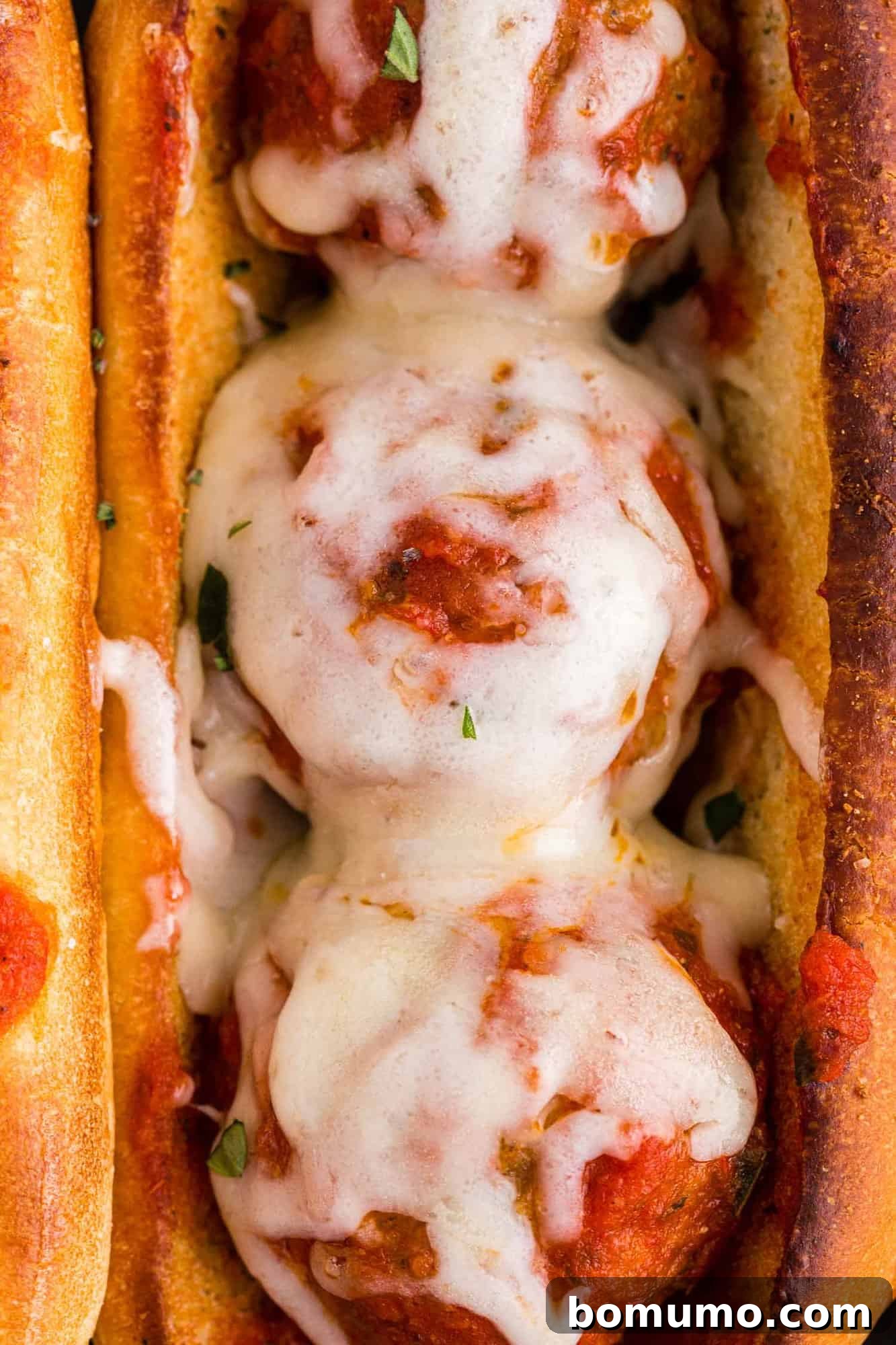 Close up of a meatball sub, showcasing melted cheese and marinara.
