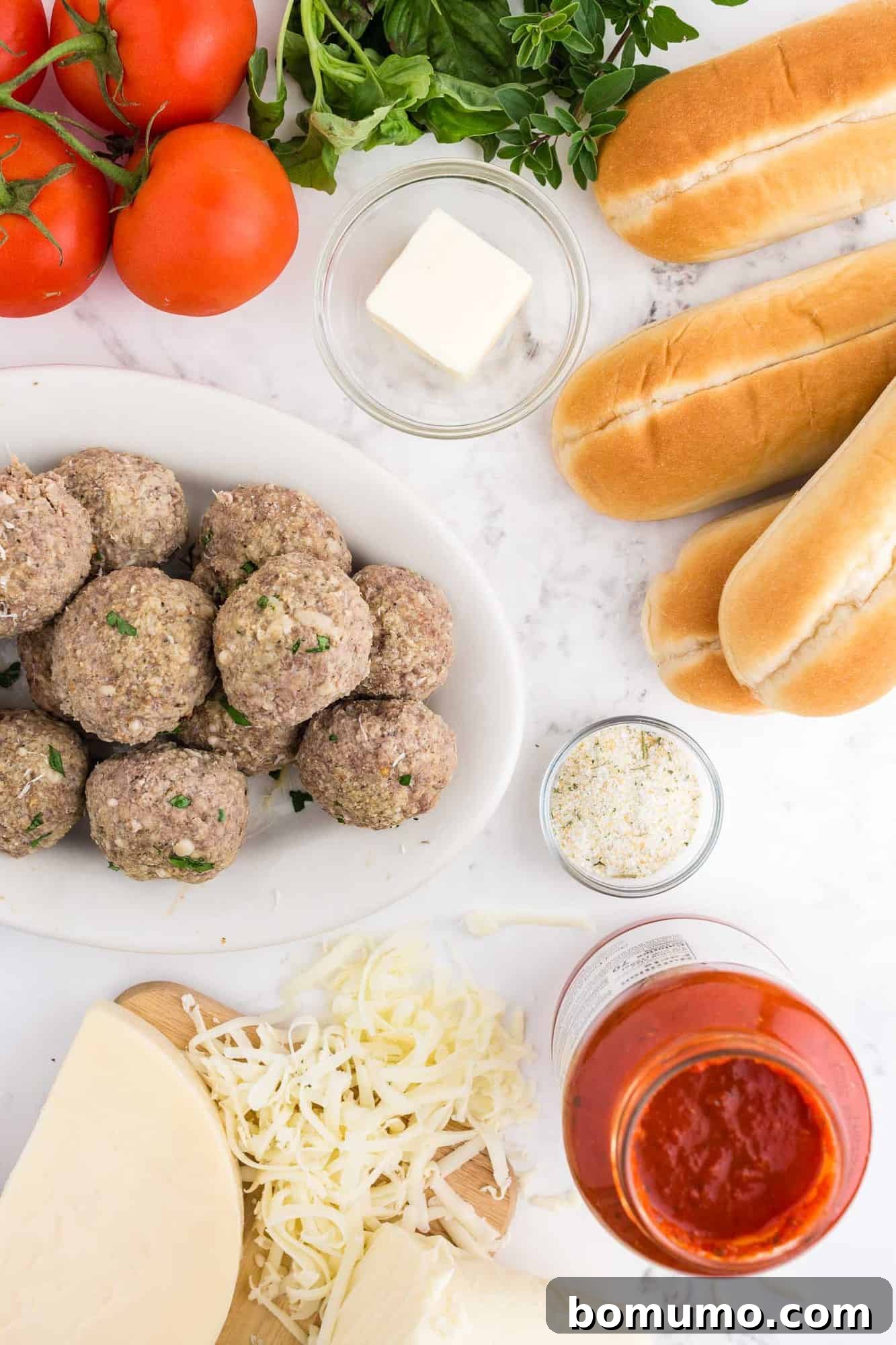 Overhead view of meatball sub ingredients: buns, meatballs, sauce, and cheese.