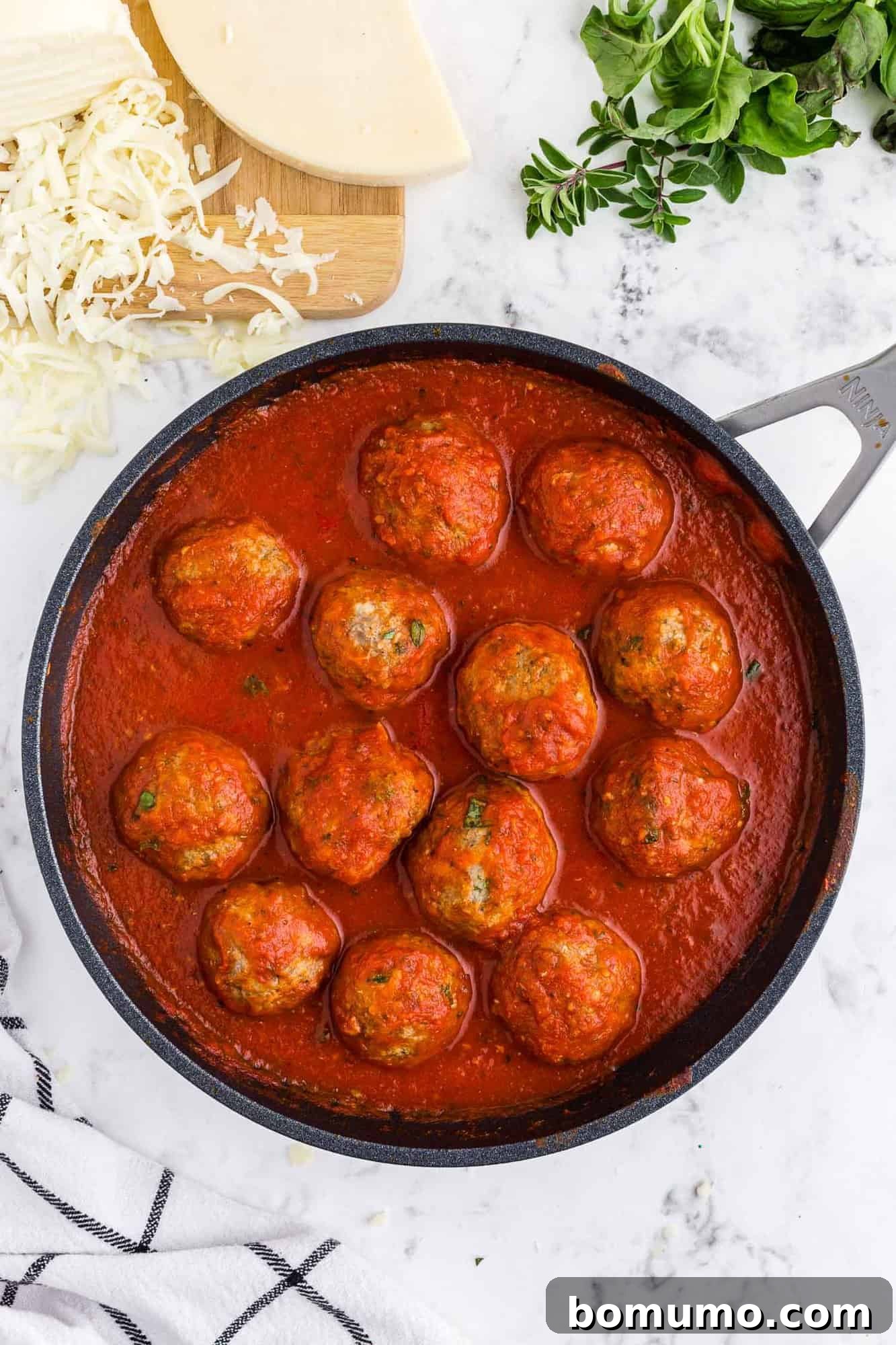 Meatballs simmering in marinara sauce in a pan.