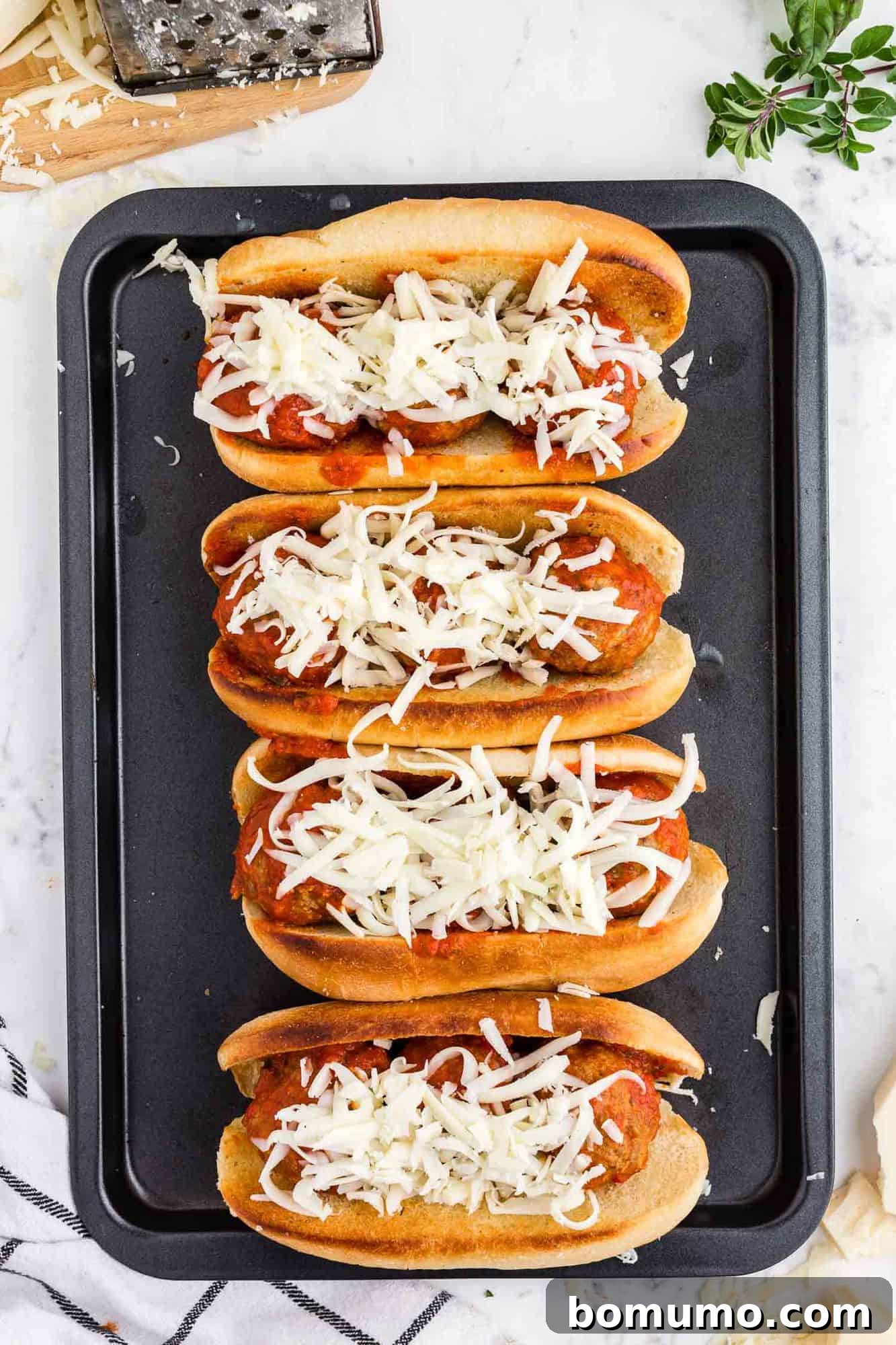 Subs with meatballs, marinara, and cheese before melting.