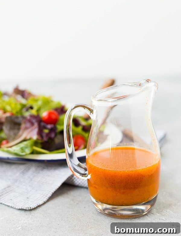 A hand pouring Carrot Vinaigrette Salad Dressing over a vibrant salad bowl filled with mixed greens, black beans, corn, and avocado, illustrating its perfect pairing with southwestern ingredients.