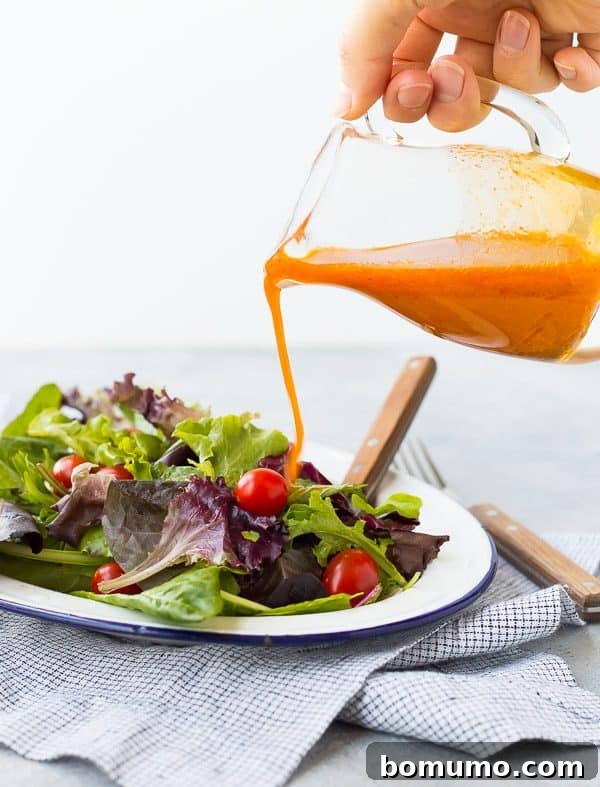 A close-up shot of a jar of Carrot Vinaigrette Salad Dressing, showing the natural separation of oil and juice, with a small whisk beside it, ready for a quick stir before serving.