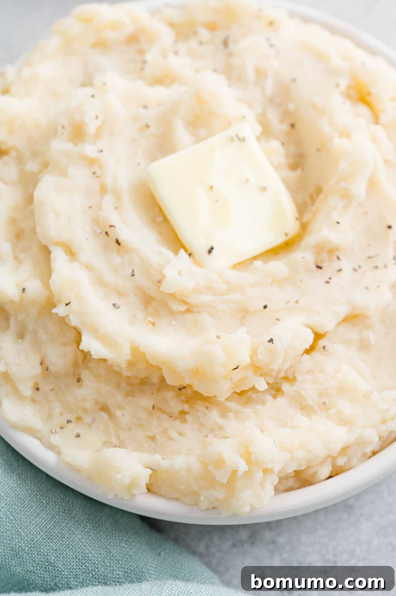 Set-It-and-Forget-It Mashed Potatoes 12 A close-up, top-down view of perfectly creamy mashed potatoes in a white bowl, garnished with a sprinkle of fresh herbs.