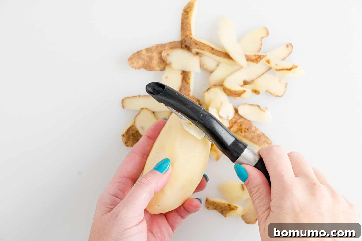 Set-It-and-Forget-It Mashed Potatoes 5 A hand using a vegetable peeler to peel a potato over a cutting board.