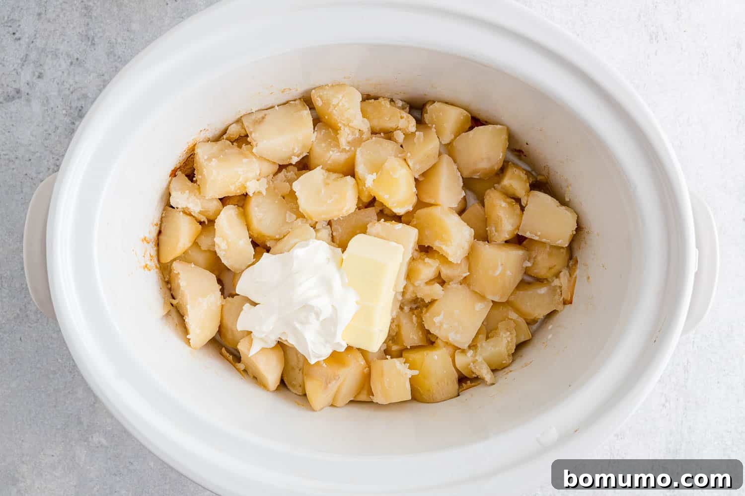 Set-It-and-Forget-It Mashed Potatoes 9 Sour cream and softened butter added to cooked potatoes in a slow cooker, ready for mashing.