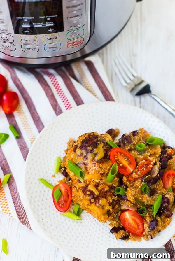 Overhead of small white plate with serving of chicken and quinoa, garnished with sliced green onions and tomatoes.
