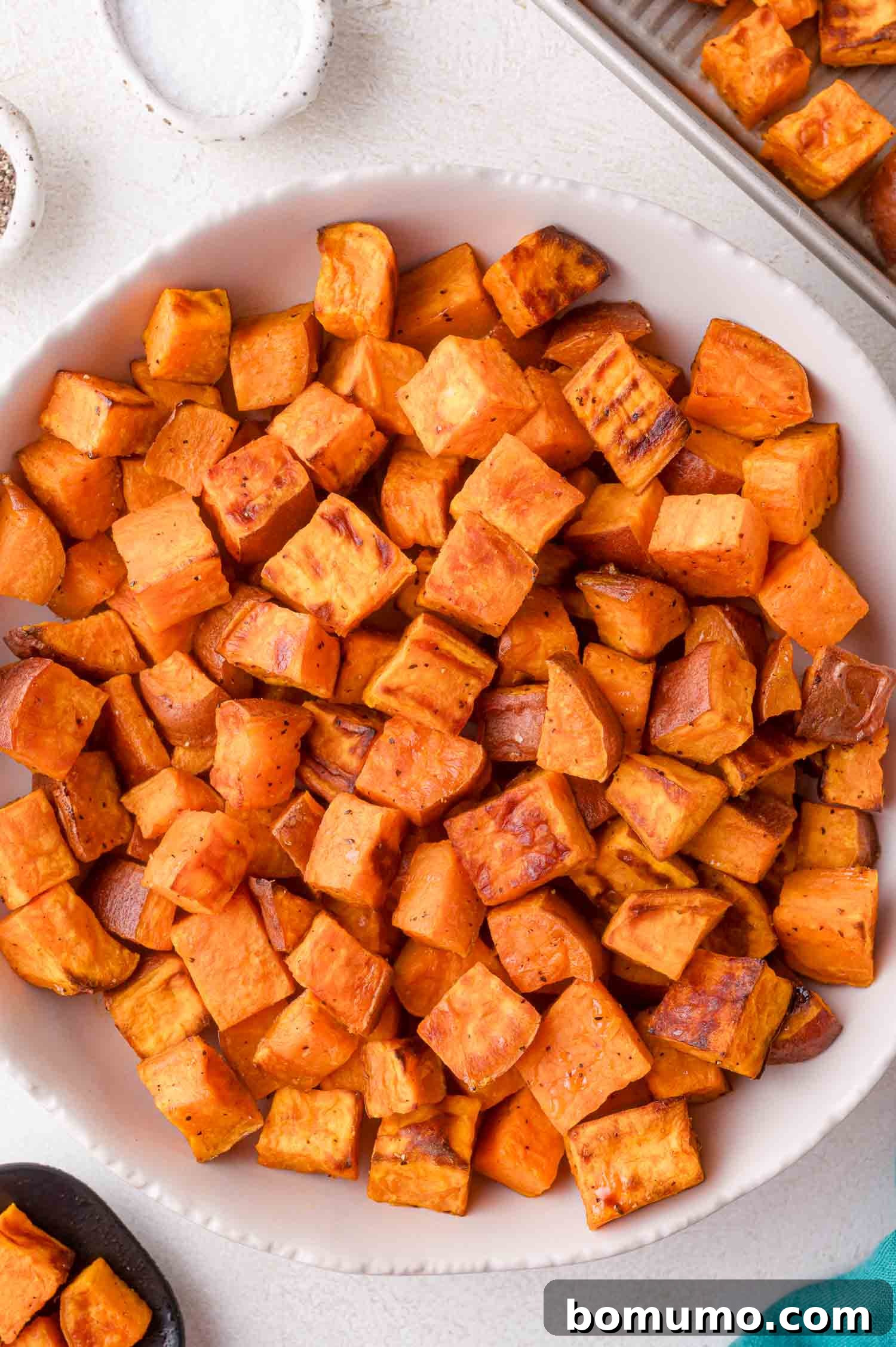 A white bowl filled with oven roasted sweet potatoes seasoned with spices, placed on a light-colored surface, ready to be served.