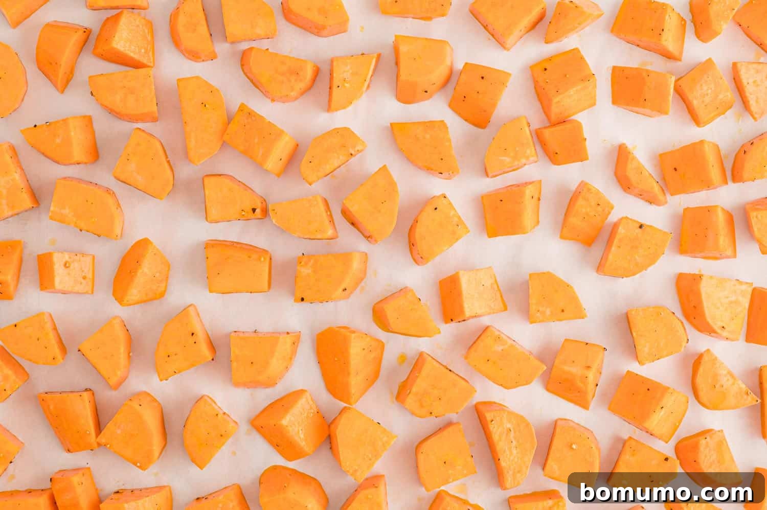 Uncooked sweet potatoes spread in a single layer on a parchment paper lined baking sheet, ready for roasting.