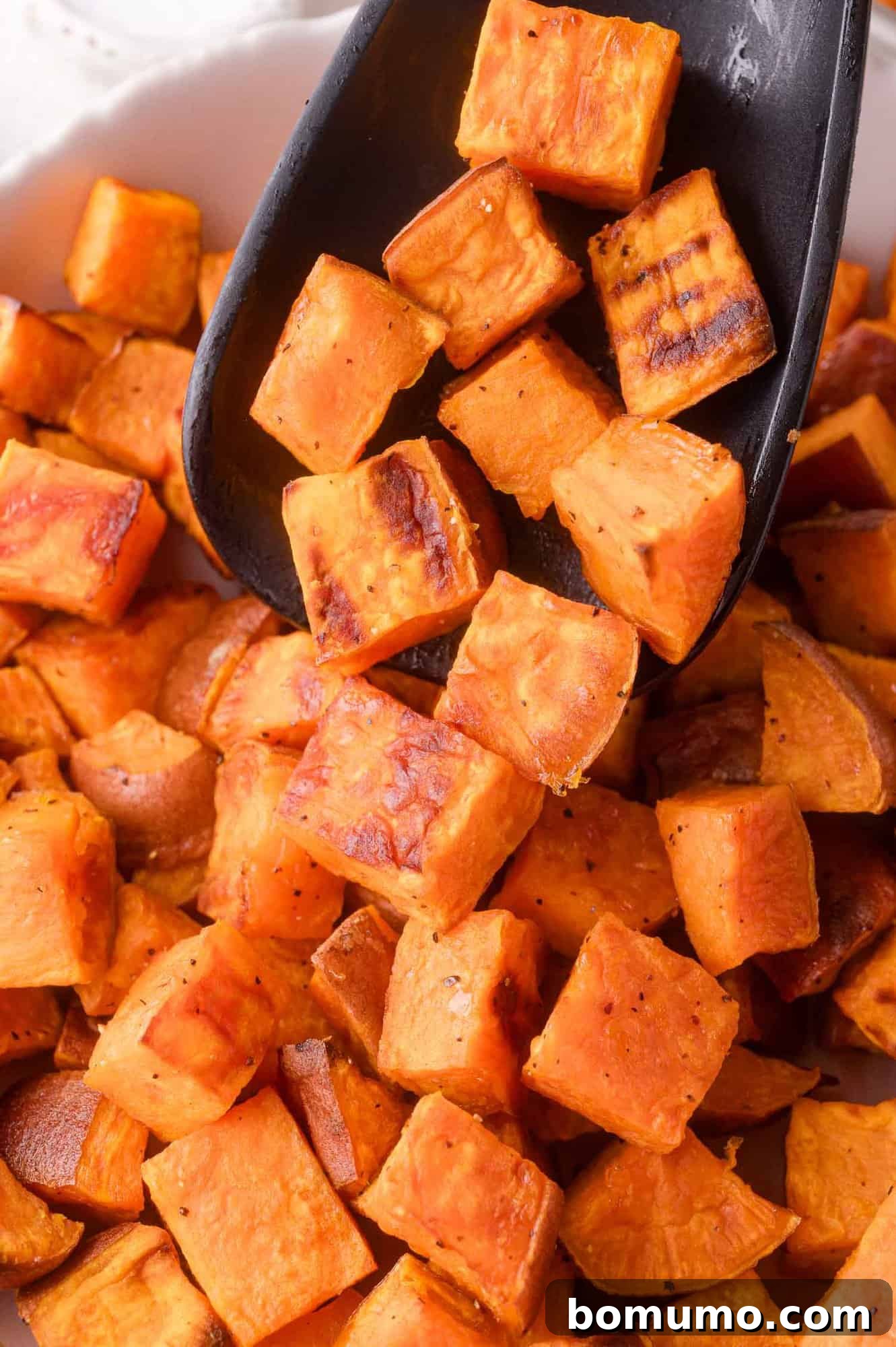 Close-up of roasted sweet potato cubes being scooped with a black spatula, ready to be served from the pan.