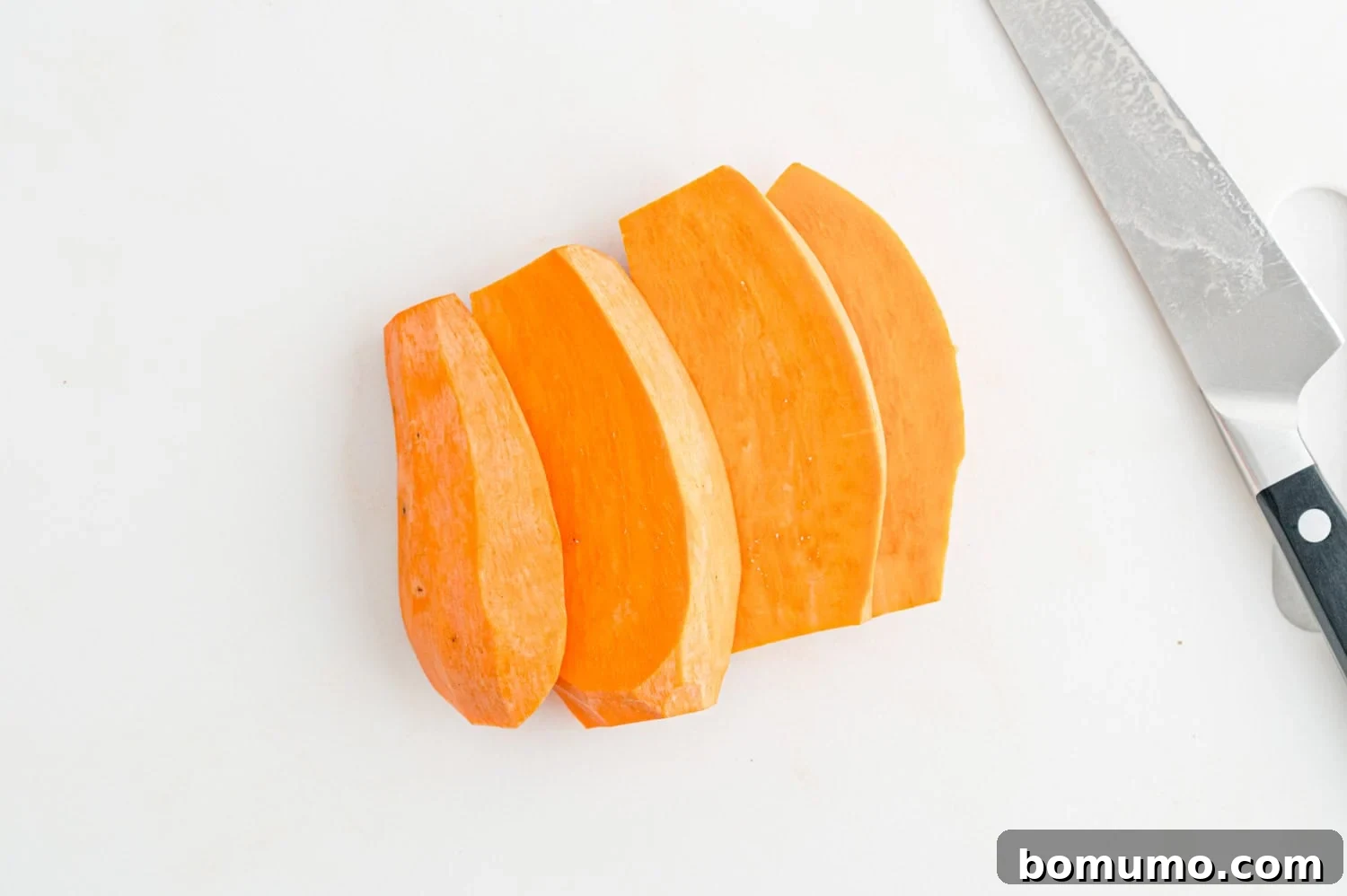 Sliced sweet potato pieces on a white cutting board next to a kitchen knife, showing preparation.