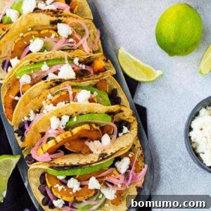 Overhead of several prepared tacos, lined up on decorative surface.