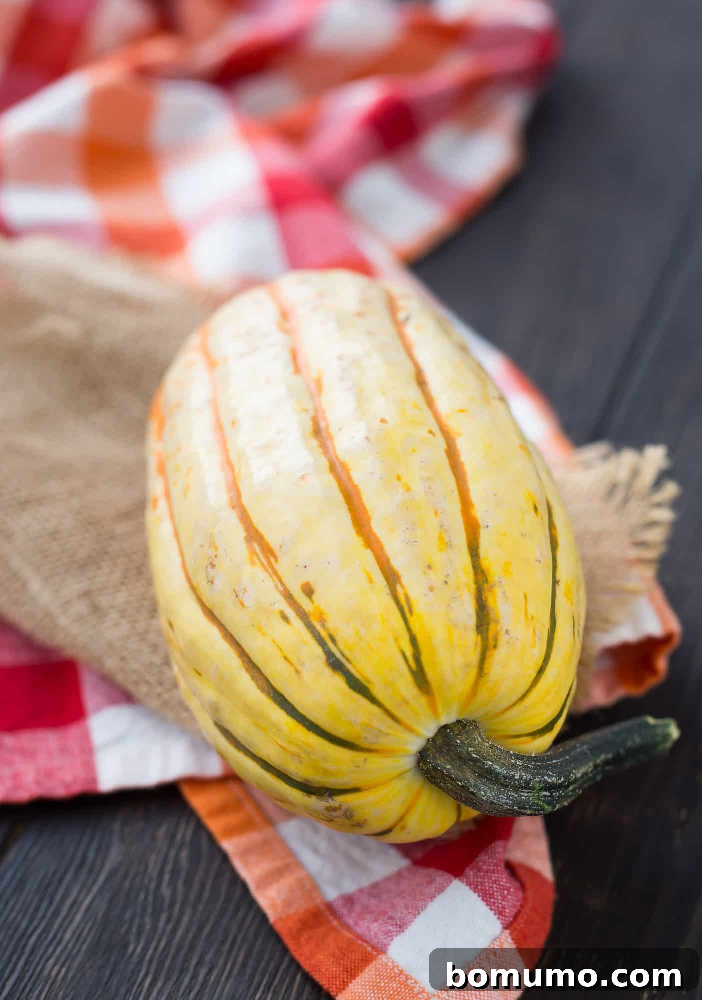 Simple Roasted Delicata Perfection 3 Uncooked, whole delicata squash on a rustic wooden surface, showcasing its signature creamy yellow skin with dark green stripes.