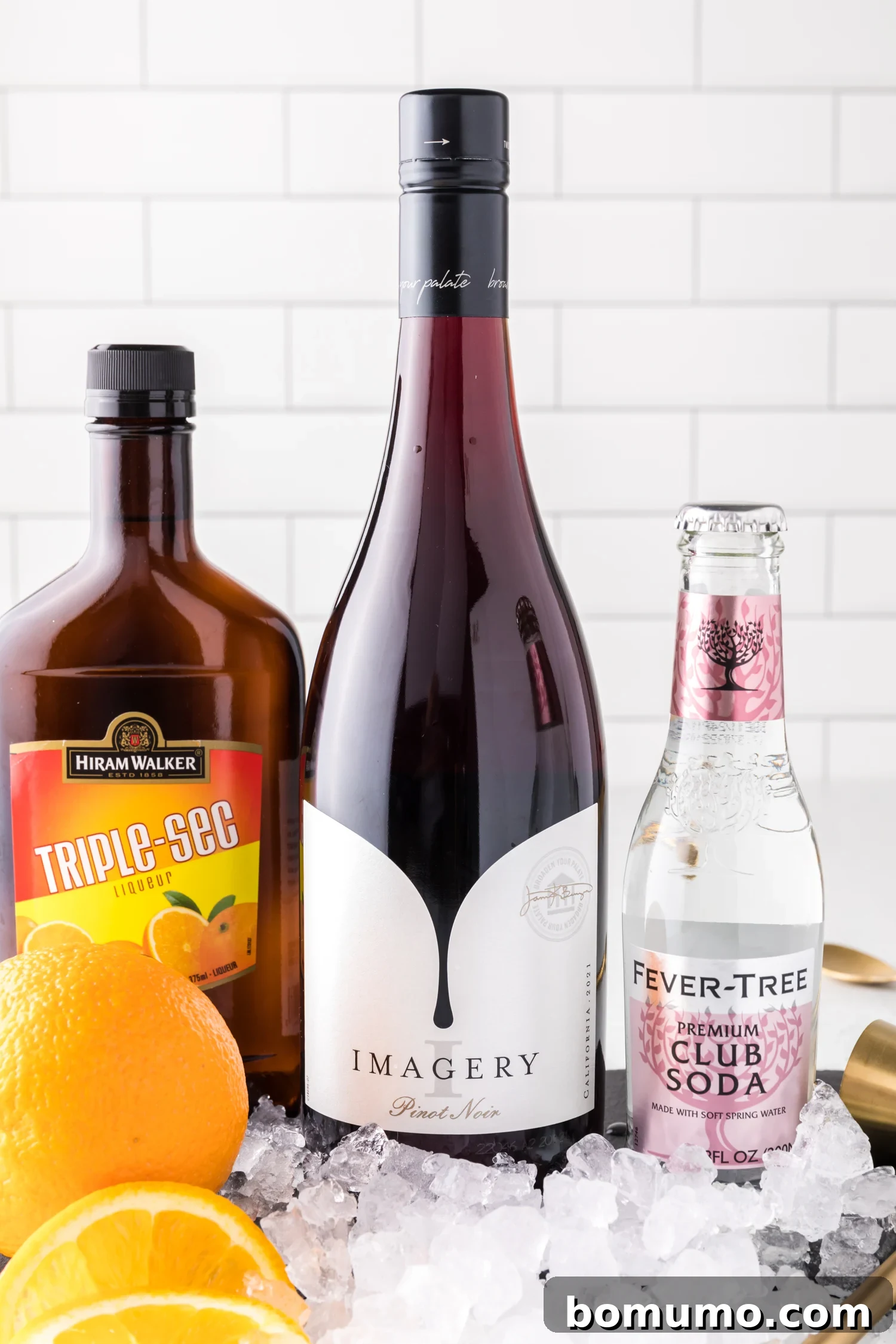 All the essential ingredients for crafting a delicious red wine spritzer laid out: red wine, orange liqueur, soda water, and fresh oranges.