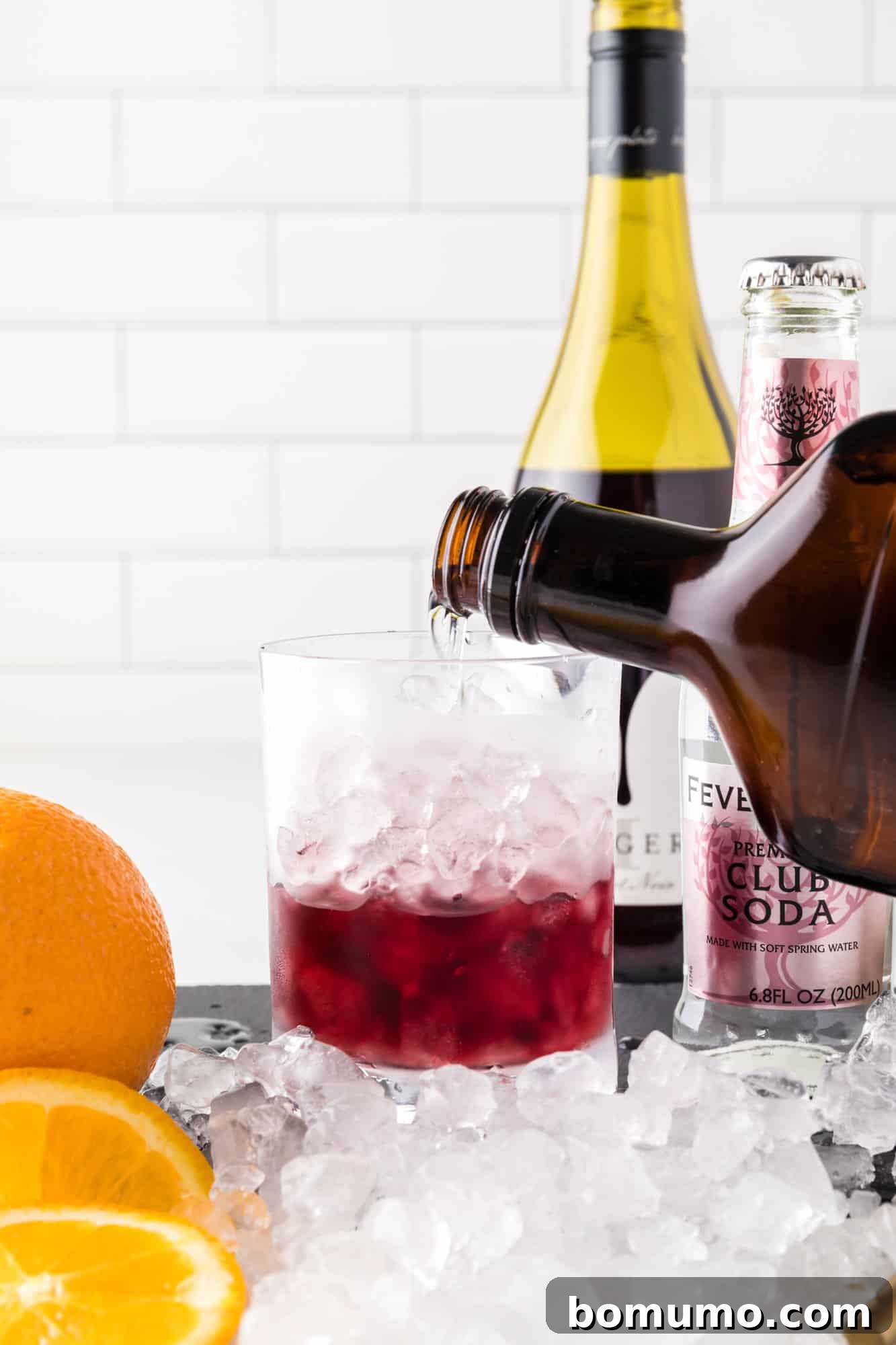 Adding orange liqueur to a glass already containing red wine and ice, to infuse citrus notes.