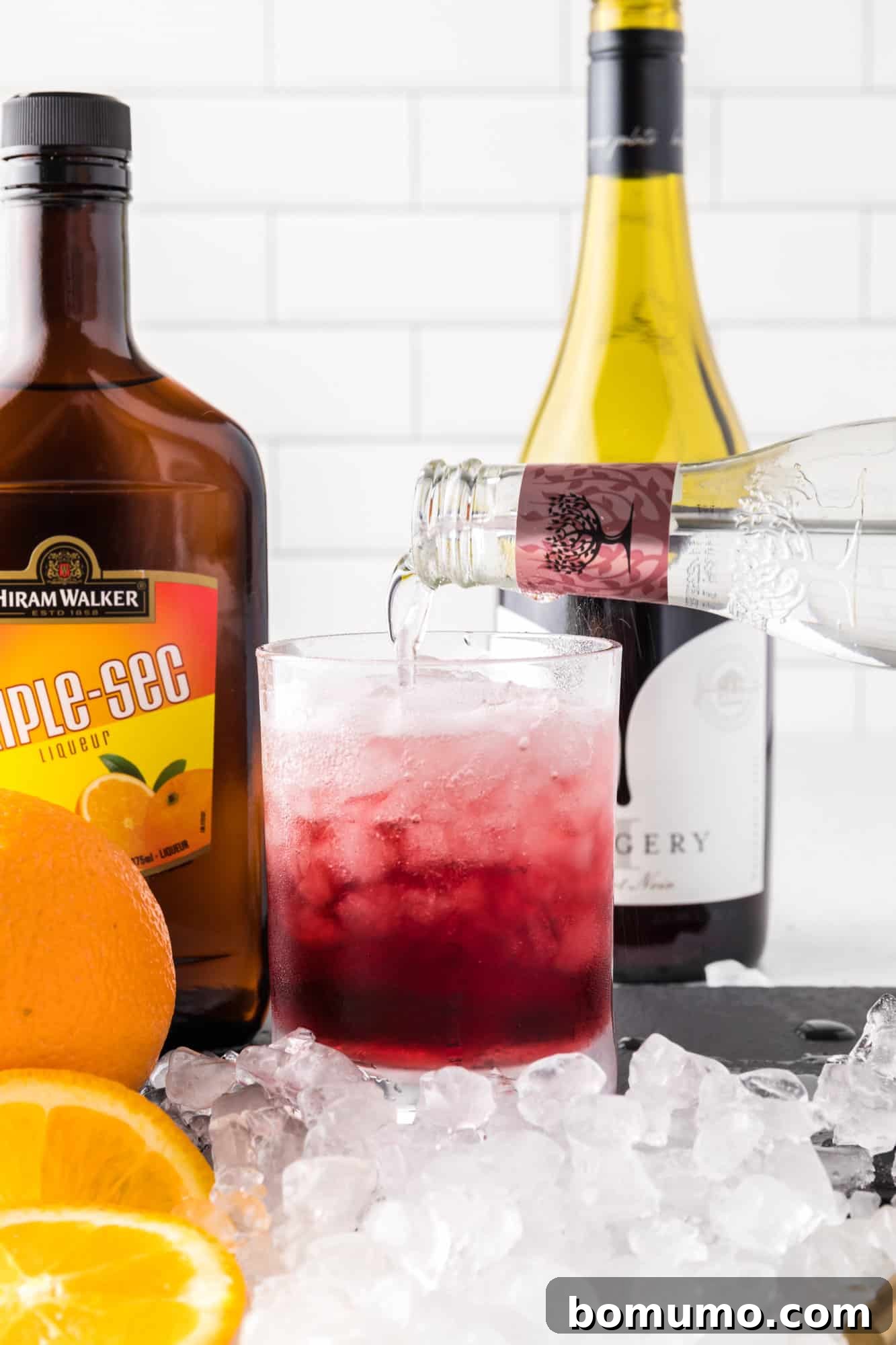 Topping the red wine and orange liqueur mixture with sparkling soda water to create the fizzy spritzer effect.