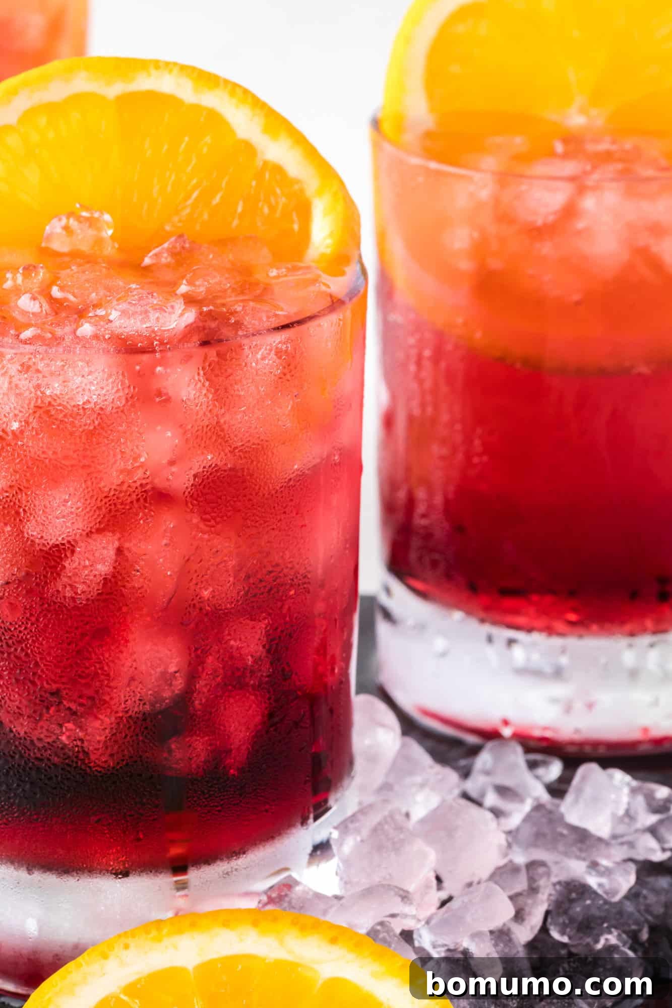 Two beautifully prepared red wine spritzers, garnished with fresh orange slices, showcasing their vibrant color and appealing effervescence.