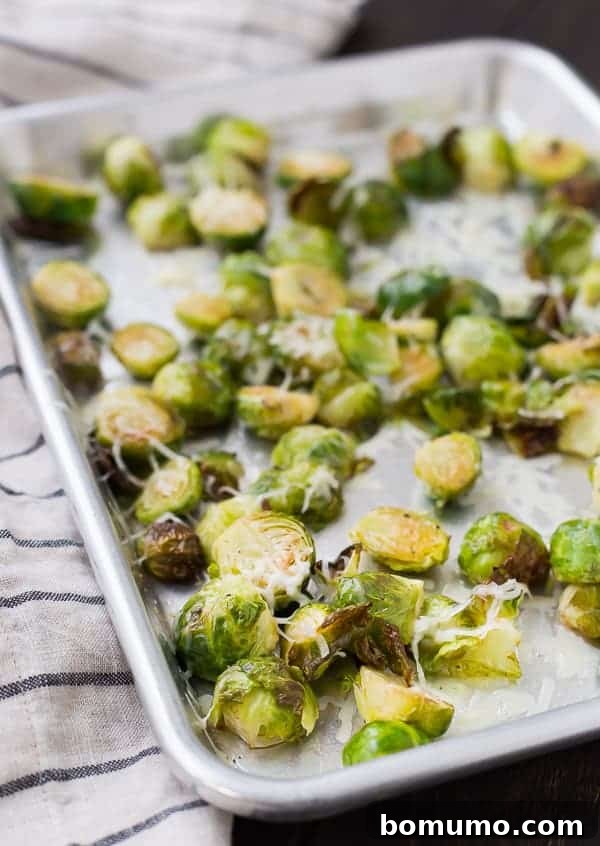 A close-up of a baking sheet filled with perfectly roasted Brussels sprouts, golden-brown and slightly charred at the edges, hinting at their delicious crispiness.