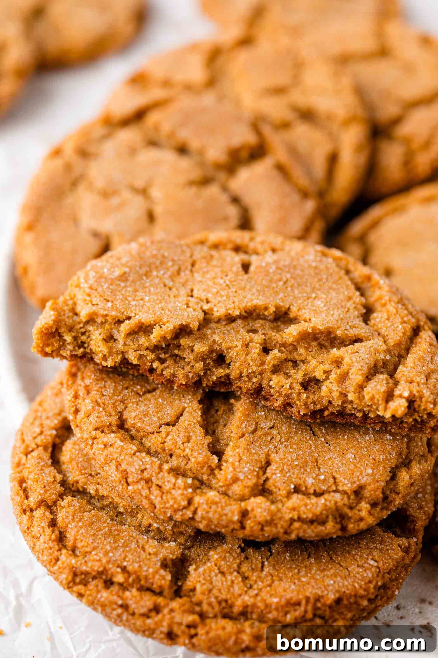 Close-up of a stack of ginger cookies, with one cookie broken in half, showing a soft, chewy interior and a beautiful sugar-coated, crackled surface.
