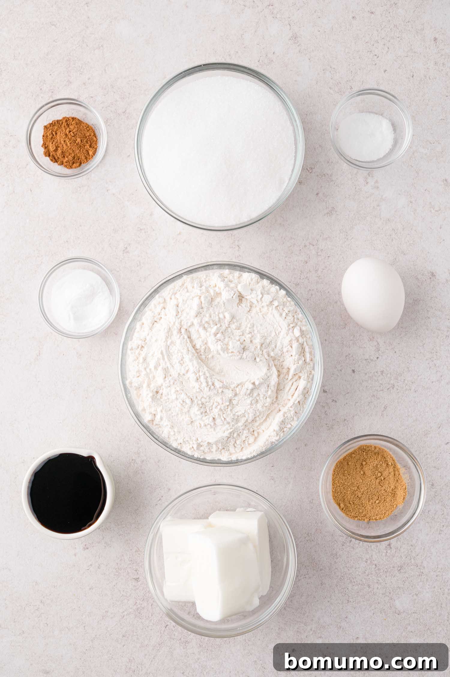 Bowls of flour, sugar, shortening, molasses, egg, baking soda, cinnamon, and salt, neatly arranged on a light surface, ready for baking.