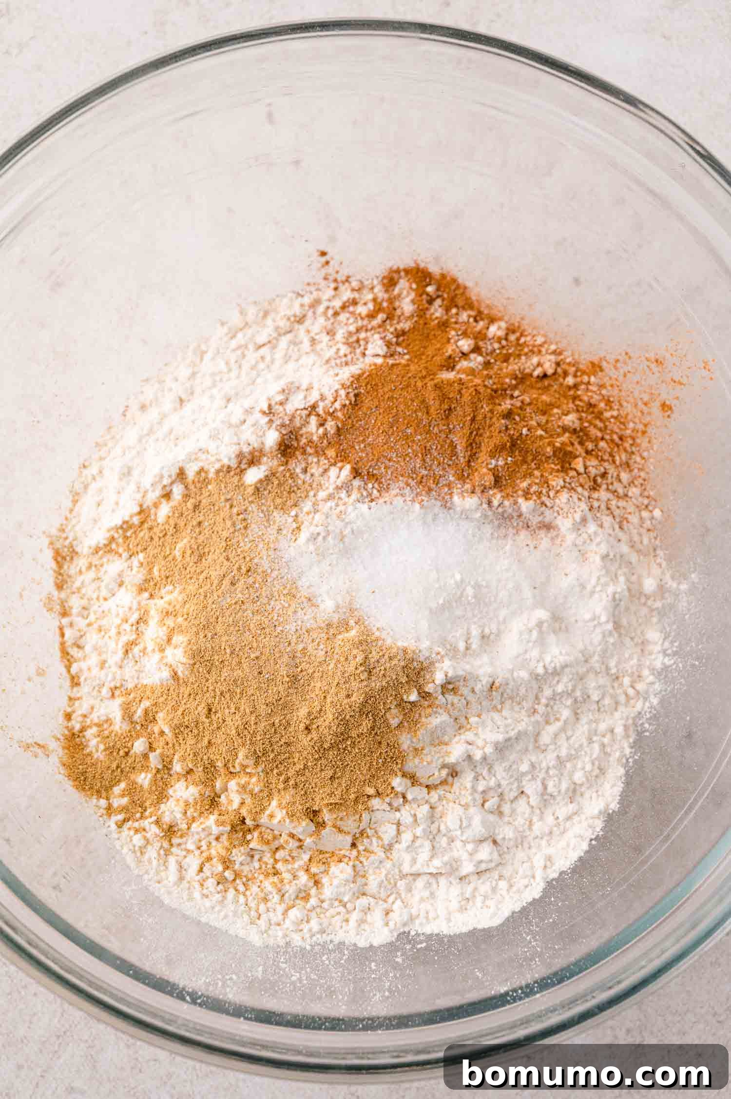 A glass bowl contains flour, baking powder, cinnamon, and nutmeg, perfectly blended dry ingredients for the cookies.